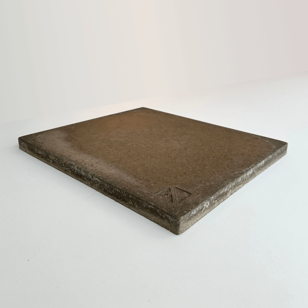 The Effeuno Biscotto Clay Pizza Stone by Effeuno is a square, flat brown tile with a slightly textured surface, set against a plain light background and featuring a small, raised triangular logo in one corner.