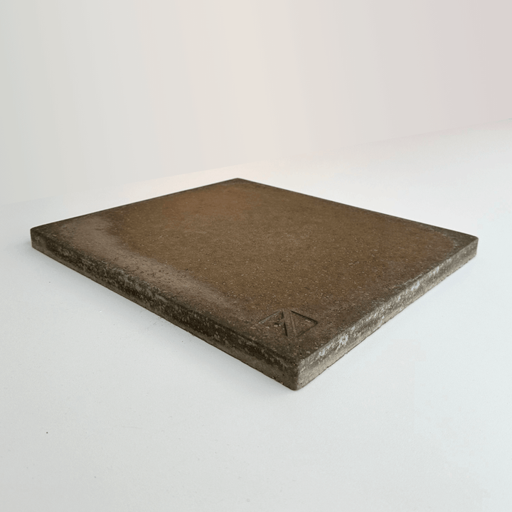 The Effeuno Biscotto Clay Pizza Stone by Effeuno is a square, flat brown tile with a slightly textured surface, set against a plain light background and featuring a small, raised triangular logo in one corner.