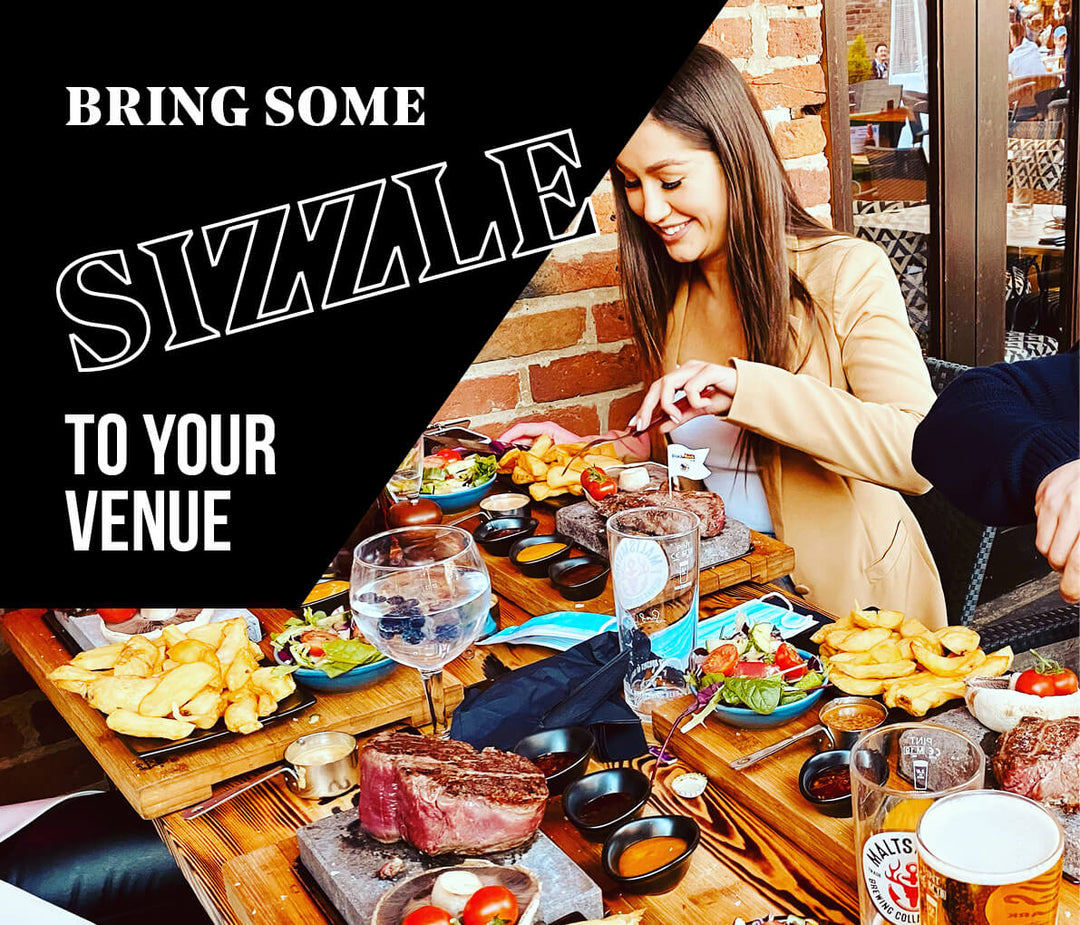 A group is enjoying meals at a restaurant with dishes like steak, fries, and vegetables on the table. The vibrant setting features brick walls and large windows. Text reads, Bring some sizzle to your venue with Black Rock Grills ROXY12 | 12 Rock, 12 Plate, Rock Oven & Accessories Set Up.