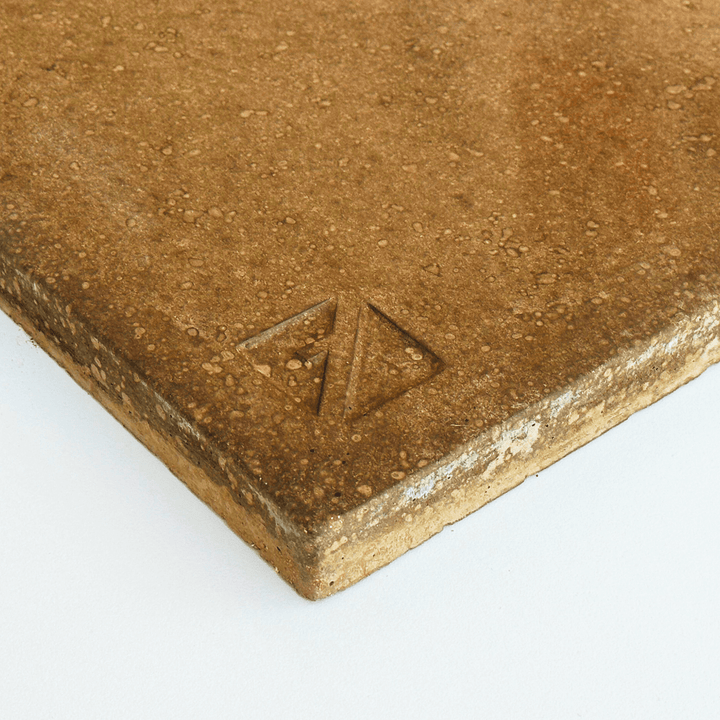 A close-up of a brown Effeuno Biscotto Clay Pizza Stone, featuring a textured surface and rounded edges with a small engraved triangular logo, set against a white background.