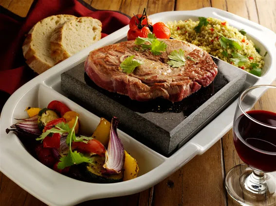 White Porcelain platter dish with steak stone in the centre with rare steak and grilled tomatoes. Side of platter holds grilled vegetables on one side and couscous on the other