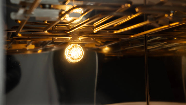 A close-up of the Effeuno Pizza Oven P134H 509 PRO + Biscotto Stone reveals glowing lights reflecting off its metal racks. The warm lighting accentuates the shiny surfaces inside this professional pizza oven by Effeuno.