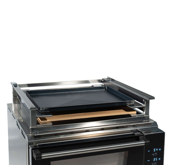 A close-up of a stainless steel oven with a digital control panel, black baking tray, brown pizza stone, and the Black Rock Grill Effeuno Stacking Kit for PRO & Evolution Ovens for safe double oven mounting.
