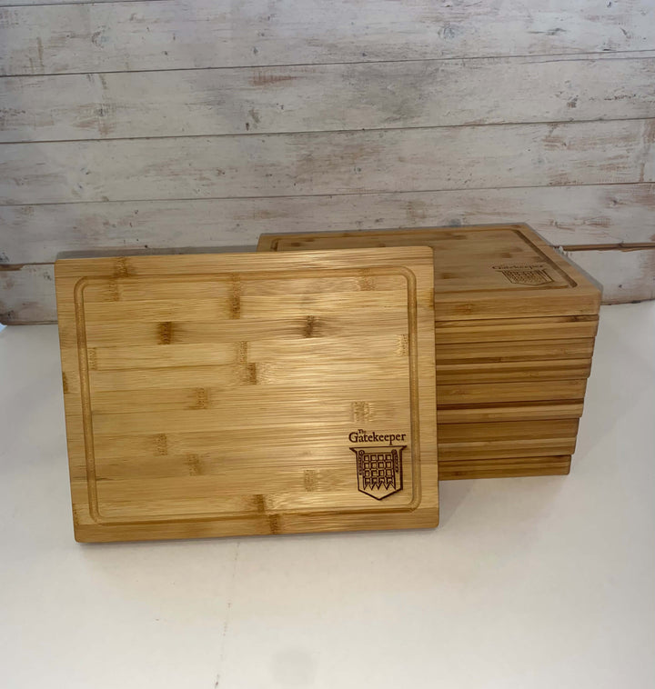 A stack of Wooden Serving Steak Boards with one upright, displaying the Black Rock Grill logo and Gatekeeper engraving. Made from sustainable bamboo, set against a light, rustic wooden background.