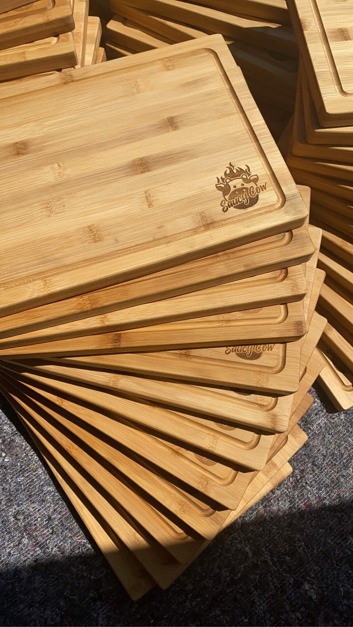 Black Rock Grills Wooden Serving Steak Boards, featuring engraved logos, shine in sunlight on a textured surface. Apply food-grade oil to preserve their beauty and durability.