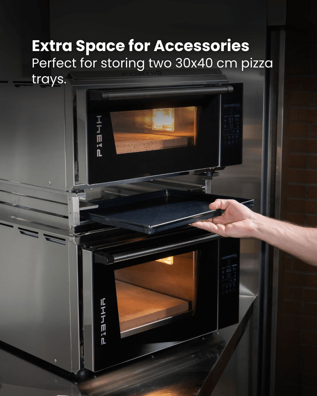 A person slides a pizza tray into an Effeuno PRO & Evolution oven with the Black Rock Grill Stacking Kit. Another oven is stacked above. Text: Extra Space for Accessories—store two 30x40 cm trays with ease.