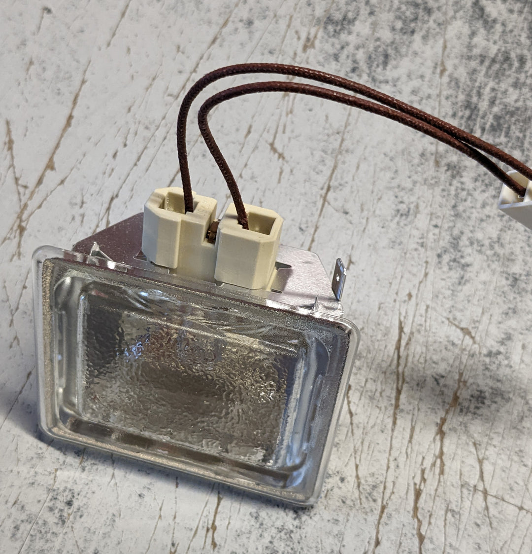 A small rectangular Effeuno Complete Lamp Holder with a flat glass shade, featuring two connected wires on top, is placed on a worn wooden surface. The metallic fixture includes plastic connectors for easy installation.