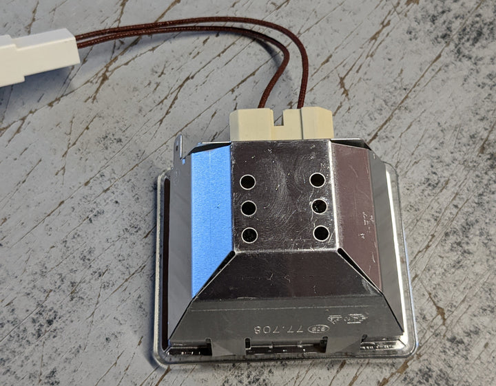 Close-up of an Effeuno Complete rectangular Lamp Holder - P134H / P134HA, a hexagonal metallic component with five circular openings and wires leading to a white connector on a scratched surface.