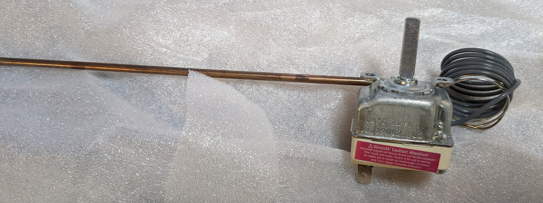 A metallic rod with a coiled wire and a small motor illustrates the Effeuno - 450°C Thermostat by Black Rock Grill. The motor, reaching up to 450°C, is mounted on packaging material, partially concealing a warning label.