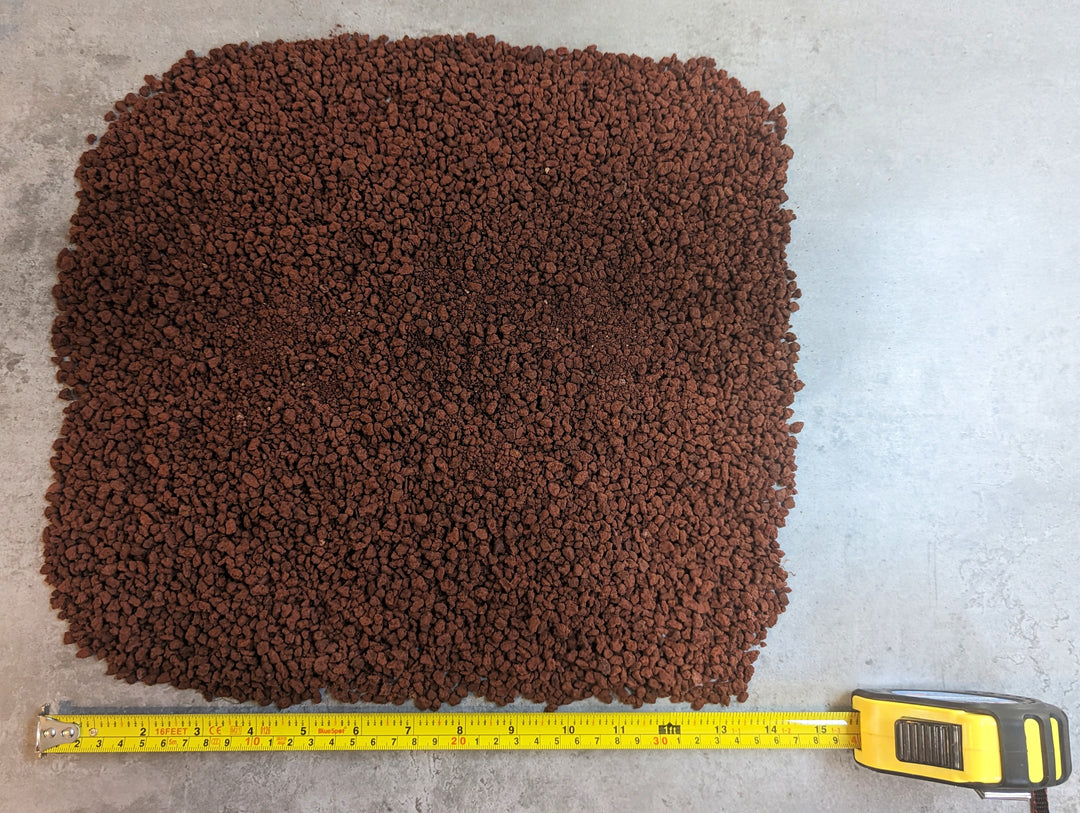 Black Rock Grills Horticulture Aquascaping Lava Rocks (2-10mm, 1KG) are spread on a gray surface. A yellow measuring tape, extended to 30cm, is placed beside the reddish-brown granules for scale.