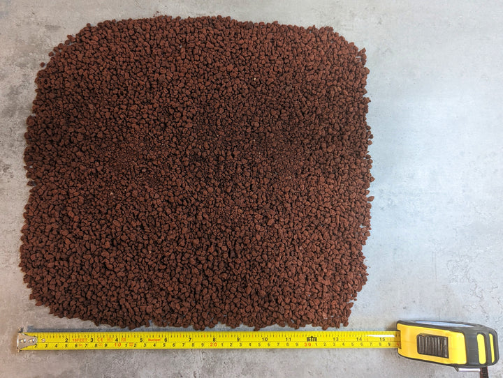 Black Rock Grills Horticulture Aquascaping Lava Rocks (2-10mm, 1KG) are spread on a gray surface. A yellow measuring tape, extended to 30cm, is placed beside the reddish-brown granules for scale.