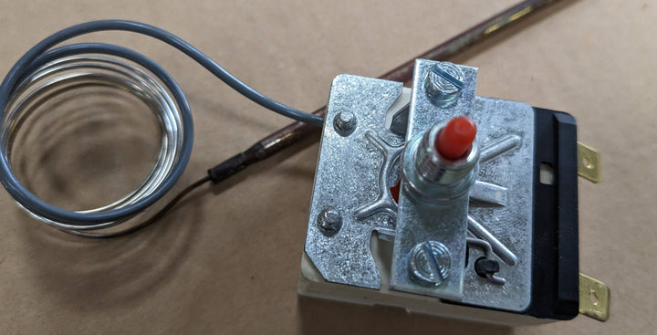 Close-up of a Black Rock Grill mechanical thermostat featuring a metal dial with a red knob and attached sensor coil, as found in Effeuno 515°C Overheat Reset Switch P134H/P134HA 450°C, 500°C, and 509°C models. The metallic casing and connectors enhance functionality against a neutral background.