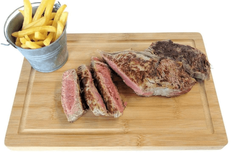 Chopping board with cooked teak chopped into pieces and small metal bucket of thin cut chips