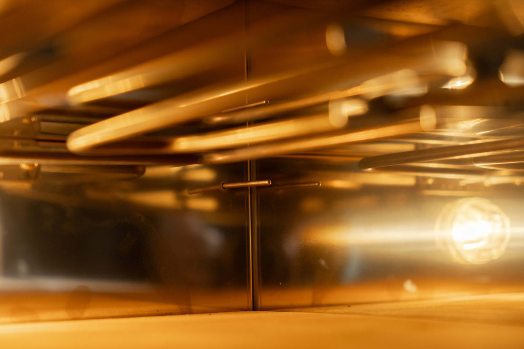 The interior of an empty, modern oven exudes professional elegance akin to Effeunos Pizza Oven P134H 509 PRO + Biscotto Stone, with warm light highlighting metal racks and reflective surfaces casting a golden glow. The geometric lines as seen from the door mirror those of the Effeuno model.
