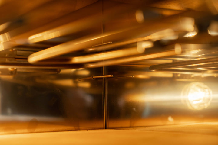The interior of an empty, modern oven exudes professional elegance akin to Effeunos Pizza Oven P134H 509 PRO + Biscotto Stone, with warm light highlighting metal racks and reflective surfaces casting a golden glow. The geometric lines as seen from the door mirror those of the Effeuno model.