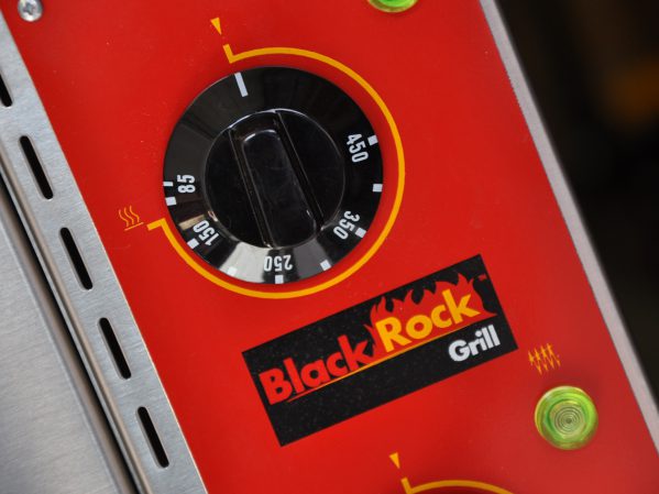 Close-up of a red dial on a Black Rock Grill device. The dial is marked with temperature settings ranging from 150 to 450 degrees. The brand logo, featuring a black and red color scheme with flames, is prominently displayed beside the dial.