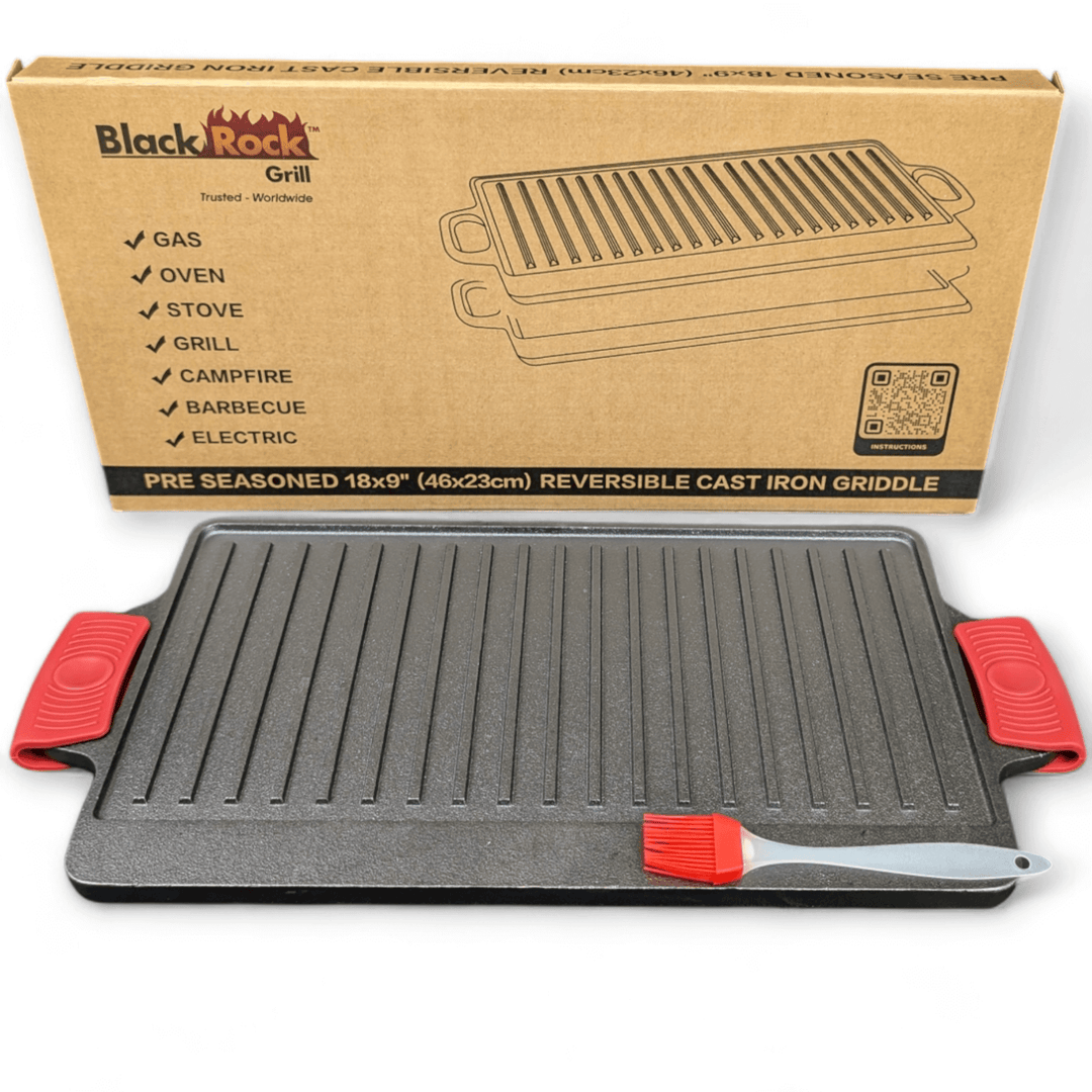 The Black Rock Grill Large Reversible Cast Iron Griddle Pan (46cm x 23cm) with red silicone grip handles and a marinating oil brush is shown in front of its box, which lists compatible heat sources for this heavy-duty BBQ griddle plate.