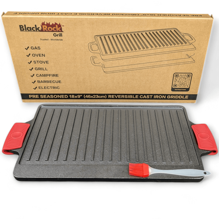 The Black Rock Grill Large Reversible Cast Iron Griddle Pan (46cm x 23cm) with red silicone grip handles and a marinating oil brush is shown in front of its box, which lists compatible heat sources for this heavy-duty BBQ griddle plate.