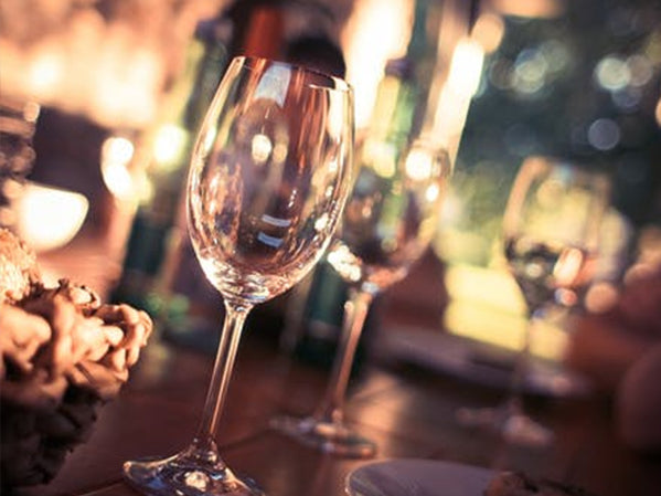 Close-up of empty wine glasses on a wooden table with warm lighting. Bottles and other blurred objects are in the background, creating a cozy, inviting atmosphere.