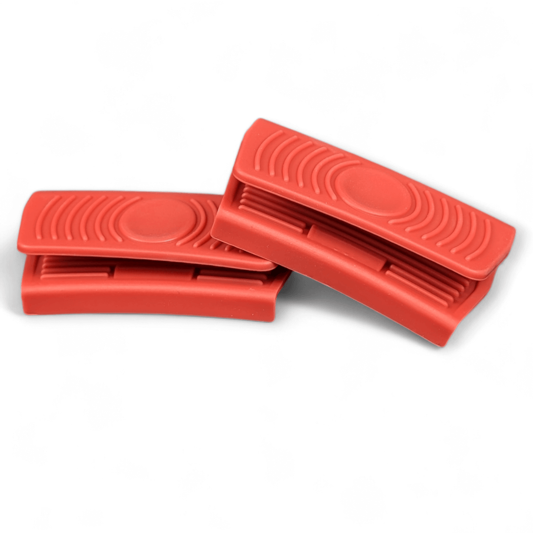 Two red silicone grip handles by Black Rock Grill overlap on a white background—perfect for securely handling your Large Reversible Cast Iron Griddle Pan (46cm x 23cm) or BBQ Griddle Plate, with included marinating oil brush.