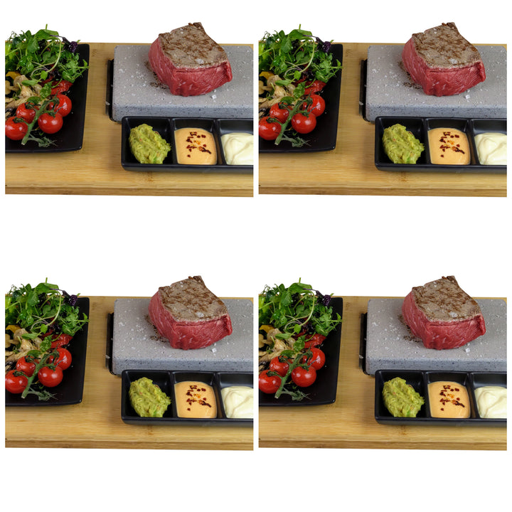 An image of a sizzling steak on the Black Rock Grill Black Steak Stone Cooking Set, served with a salad of cherry tomatoes and mixed greens. A side tray offers guacamole, sauce, and bread. This setup on a wooden surface provides an ideal healthy dining experience.