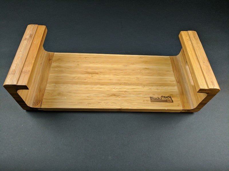 A bamboo rack bathtub tray featuring handles and a natural finish, adorned with the Black Rock Grill logo. This Replacement Bamboo Rack for Sharing Stone Set adds minimalist style to a dark backdrop while offering functionality.