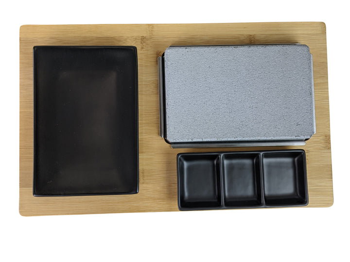 The Black Rock Grill Black Steak Stone Cooking Set features a rectangular bamboo board holding a large black rectangular plate, a hot stone slab for cooking, and three small black square dishes, ideal for healthy dining.