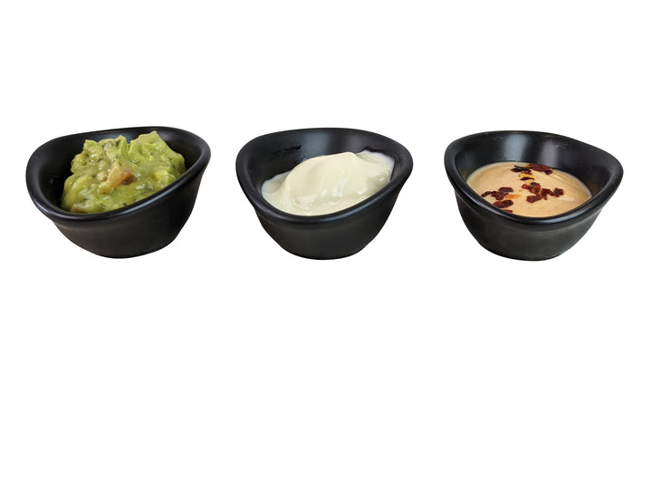 Three Black Rock Grill matt black porcelain ramekin dipping pots are lined up on a white surface, containing guacamole, sour cream, and a creamy sauce with red seasoning.