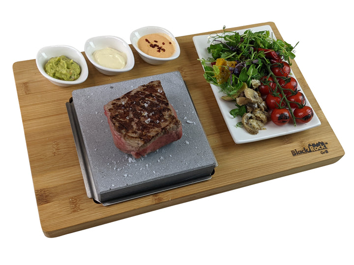 The Black Rock Grill Steak On The Stone Set by Black Rock Grill offers a unique dining experience with a seared steak on a hot stone, three sauce dishes, and a fresh salad with cherry tomatoes, mixed greens, and mushrooms.