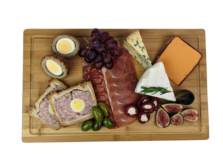 Black Rock Grills large wooden serving board showcases a delightful assortment: two scotch eggs, purple grapes, blue and soft cheeses, sausage slices, pâté with egg, figs, olives, and cheese-stuffed peppers. Ideal for gatherings or special occasions.