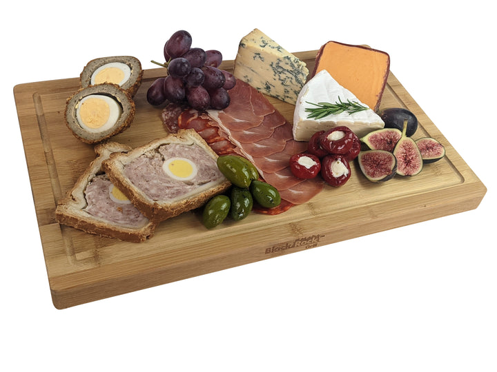 Black Rock Grills Large Wooden Serving Board beautifully displays cured meats, blue cheese, soft cheese, stuffed peppers, green olives, halved Scotch eggs, pork pie slices, figs, goat cheese with rosemary, and a bunch of purple grapes—ideal for custom laser engraving.