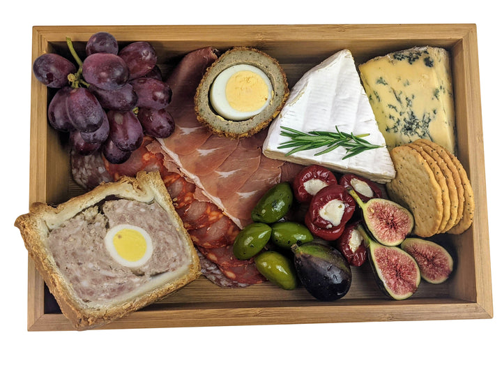 The Black Rock Grill Bamboo Wooden food presentation tray beautifully displays items like sliced meats, blue cheese, brie, pâté, boiled eggs, figs, red grapes, olives, stuffed peppers, and crackers—all elegantly garnished with rosemary for stunning presentation.