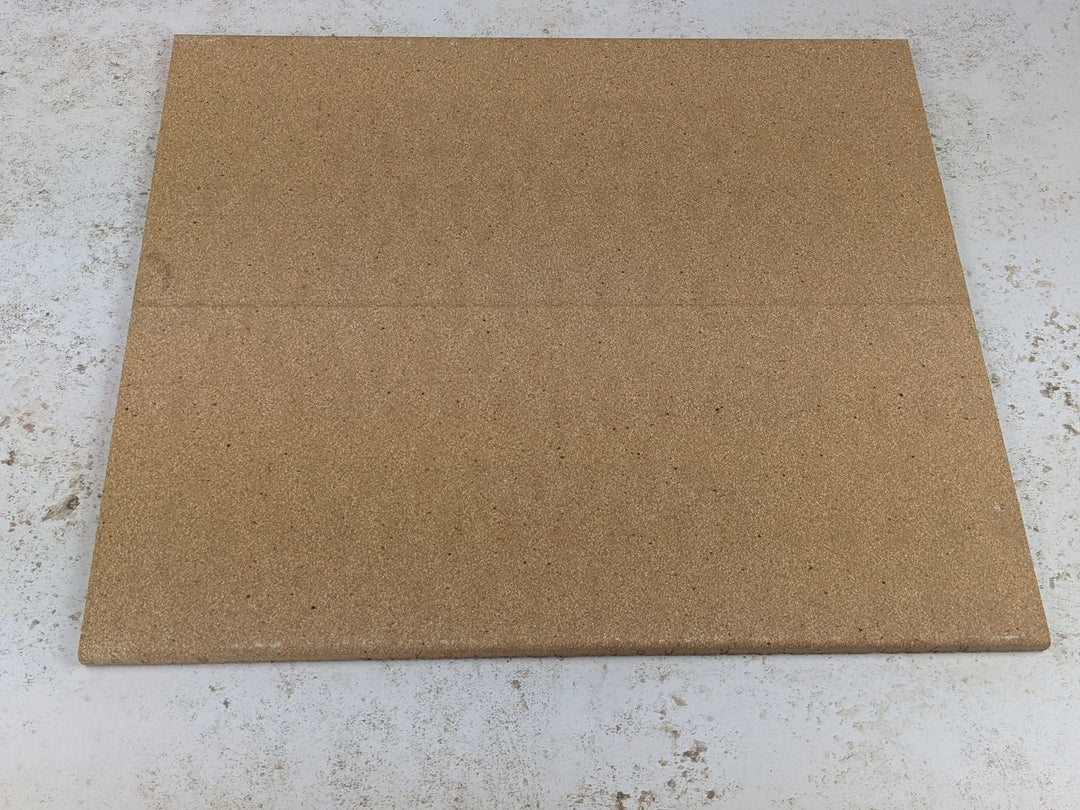 A square corkboard lies on a light, speckled surface similar to the texture of a Black Rock Grill Refractory Stone for Pizza Oven. The board is plain with a subtle seam across the middle.