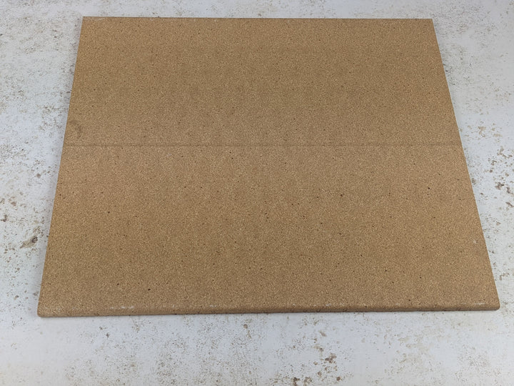 A square corkboard lies on a light, speckled surface similar to the texture of a Black Rock Grill Refractory Stone for Pizza Oven. The board is plain with a subtle seam across the middle.
