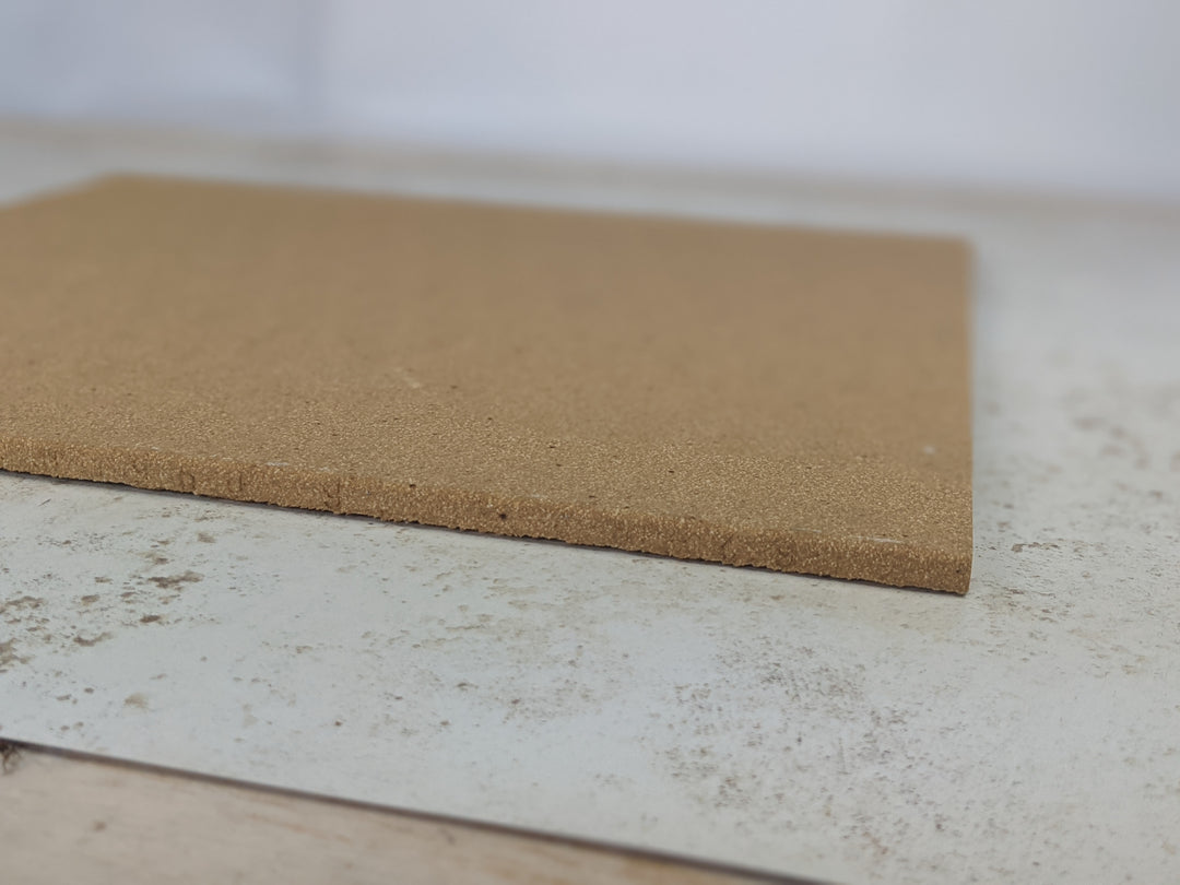A flat, rectangular Refractory Stone for Pizza Oven by Black Rock Grill lays on a speckled white and gray surface reminiscent of a Roxy 12 oven. The blurred, light background suggests an indoor setting. The stone appears unused and in good condition.