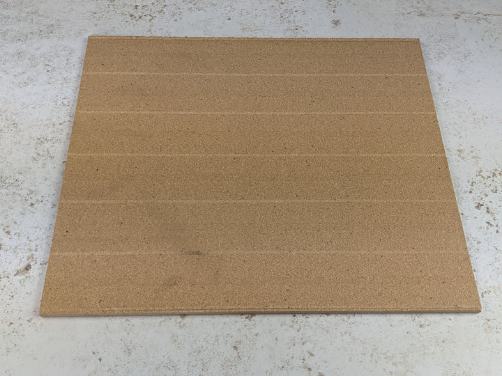 A large, square corkboard sits on a speckled surface, similar to the cooking area of a Black Rock Grill Refractory Stone for Pizza Oven. The faint horizontal lines across the corkboard create sections reminiscent of sliced crispy stone-baked pizza.