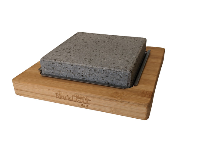 The Black Rock Grills NEW Lava Stone Steak Multi Pack features a square lava stone slab with a rough, speckled texture, elegantly elevated on a rectangular wooden board. The board has an engraved logo and is perfect for hot stone cooking. It is isolated against a plain white background.