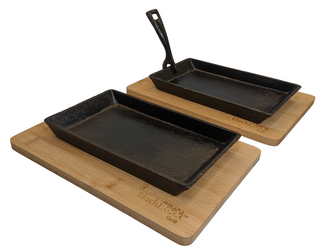 Two Black Rock Grill cast iron rectangular skillets sit on wooden boards against a plain white background, embossed with the brands logo. One skillet includes a sleek handle, while the other does not.