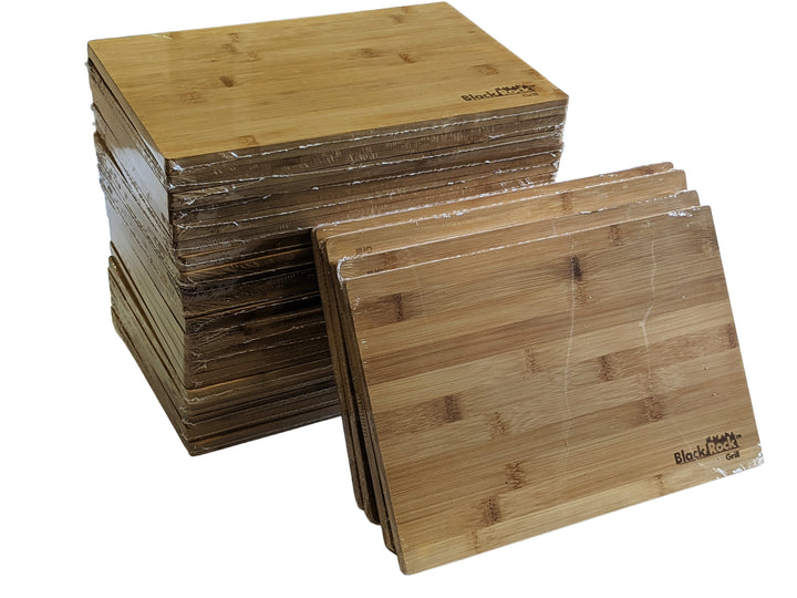 A stack of Black Rock Grill wooden serving boards (30 x 20 x 1.2cm) is shown, with several leaning against it. They feature a natural wood grain and custom laser engraving in the corner, all wrapped in plastic packaging.