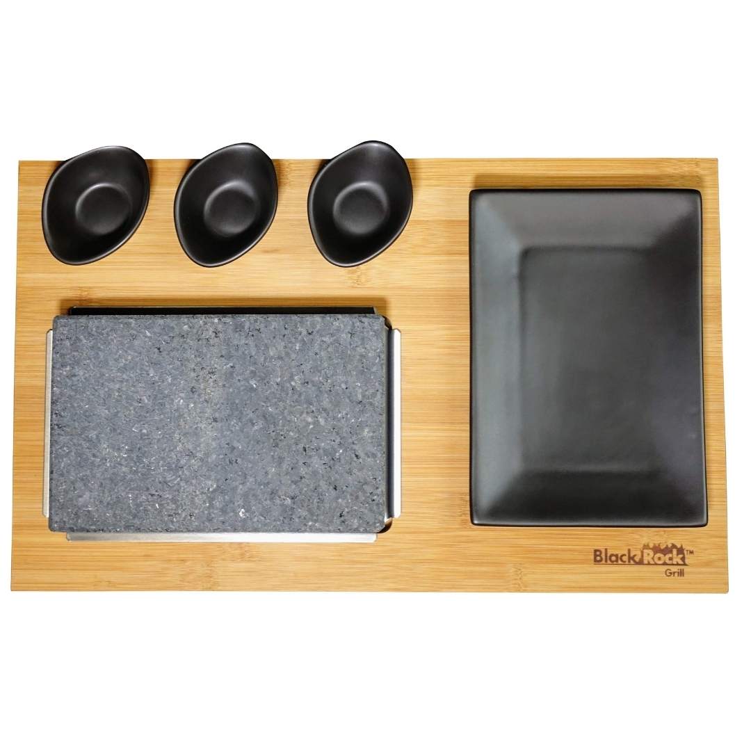 The elegant bamboo serving board from Black Rock Grills Matt Black Range includes a left-side stone slab for Steak on the Stone, a right-side black rectangular plate, and three top black bowls. The Black Rock Grill logo is engraved at the bottom right.