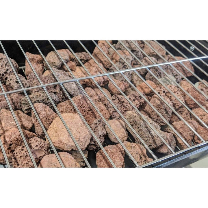 A close-up of a barbecue grill showing Black Rock Grill's Lava Rocks for Grilling (4-8cm / 40-80mm) beneath the metal grate inside the gas BBQ chamber.