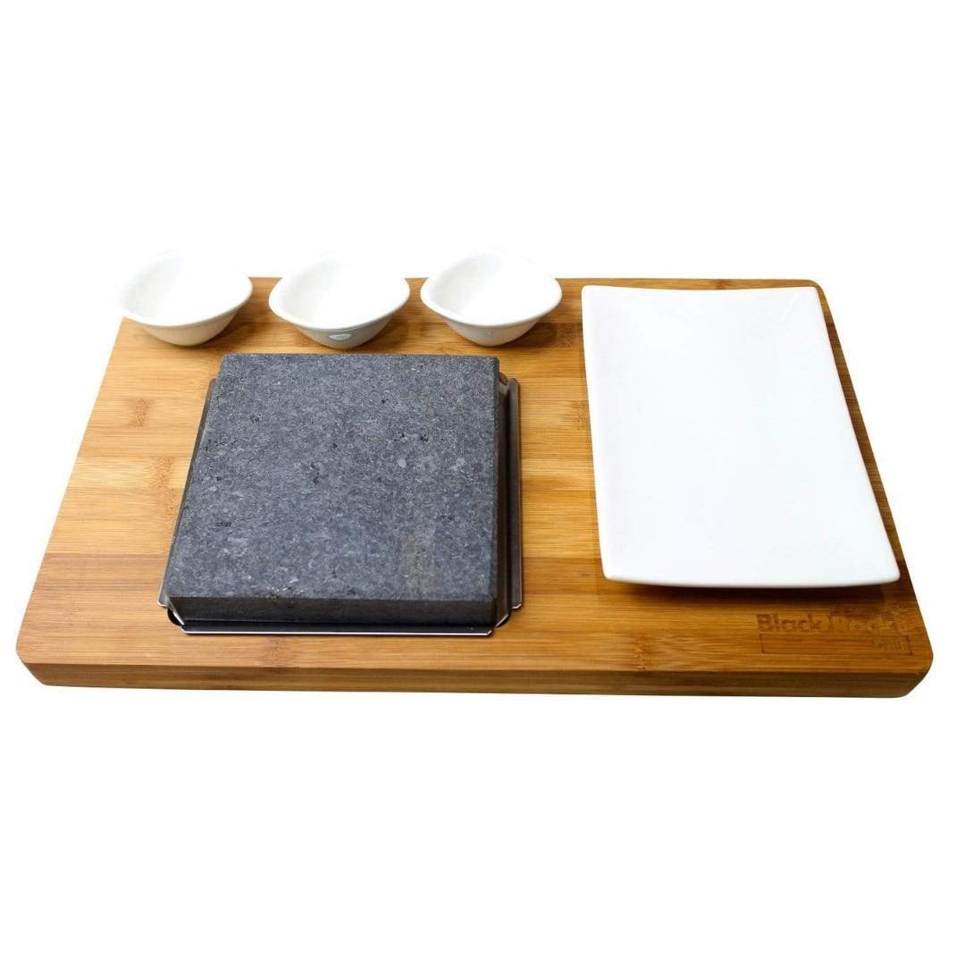 The Black Rock Grill Steak on the Stone Gift Set includes a bamboo board with a rectangular stone slab, a white plate, and three small bowls—ideal for steak enthusiasts who seek elegance in hot rock grilling.