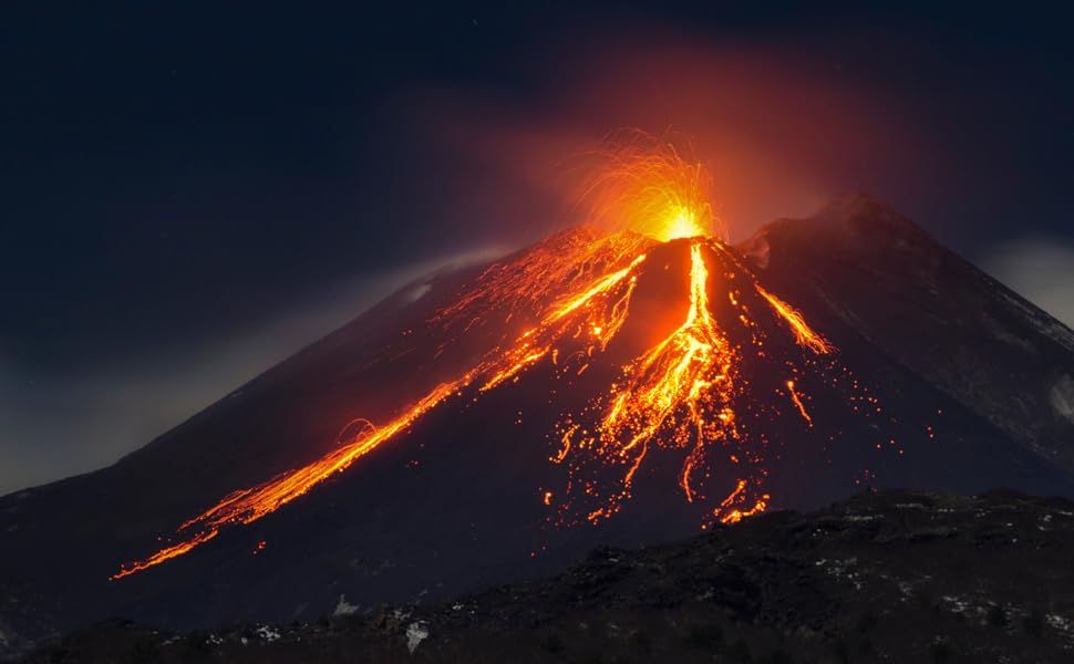 A volcano erupting in the night lava visibly flows brightly down the side of the peak.