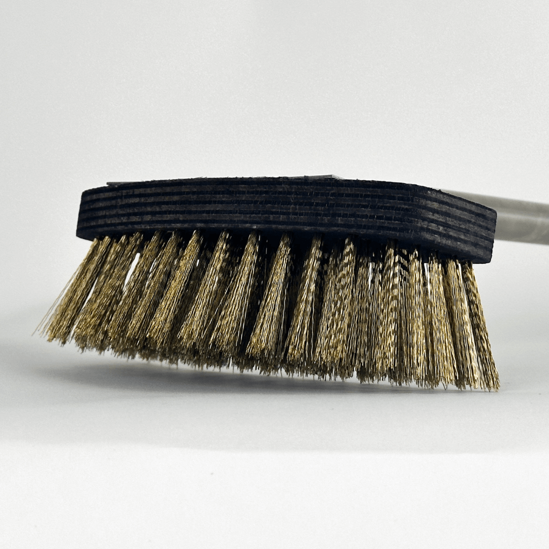 A close-up of the Effeuno Pizza Oven Brush highlights its dense brass bristles and dark, long handle. The brush, designed for safe cleaning, is tilted against a plain white background, showcasing the sturdy metal bristles.