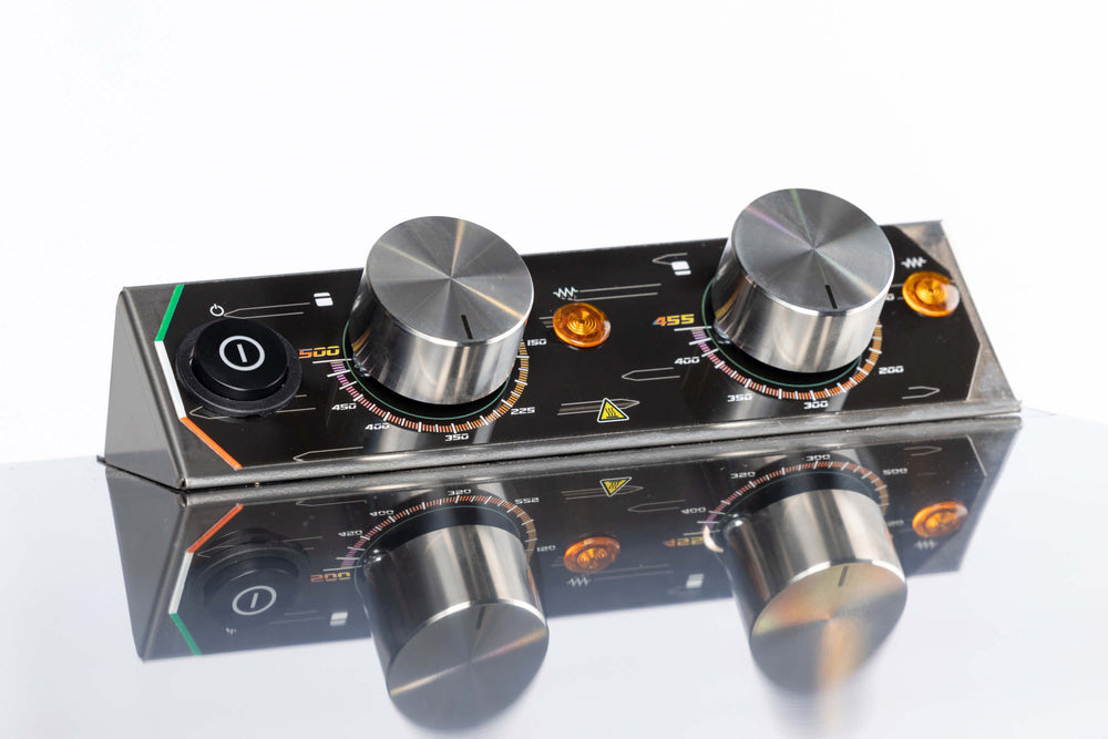 A close-up of the Macte Voyager Twin Electric Pizza Oven's control panel shows two large metal knobs, colored indicator lights, a power switch, and measurement markings reflected on a shiny surface. AVPN Certified Italian Countertop Oven by Macte.