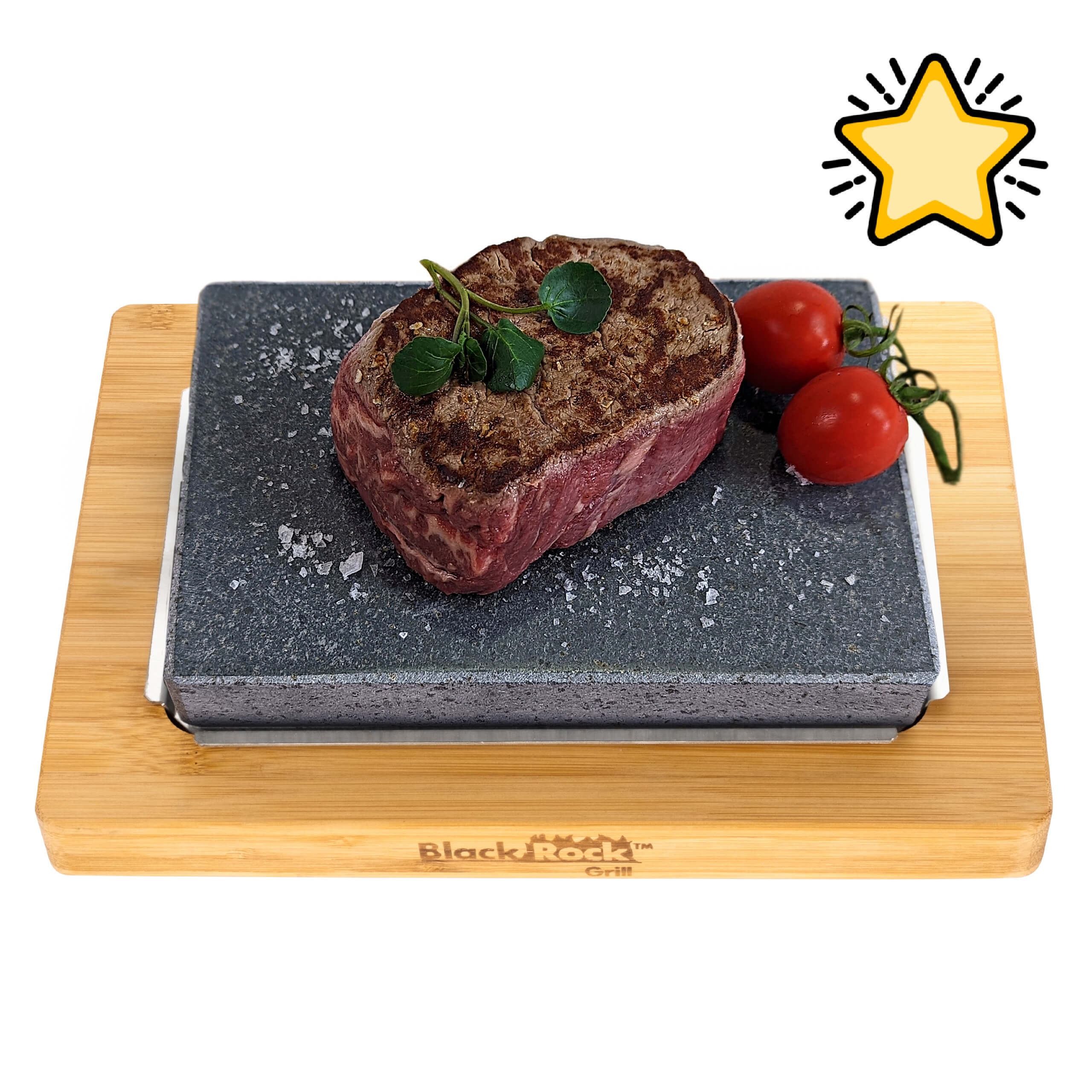A seared steak with herbs and sea salt sits on a hot stone slab from the Black Rock Grill Steak Stone Cooking Set, with two vine tomatoes on a bamboo board labeled Black Rock Grill. A yellow star decorates the top right corner.