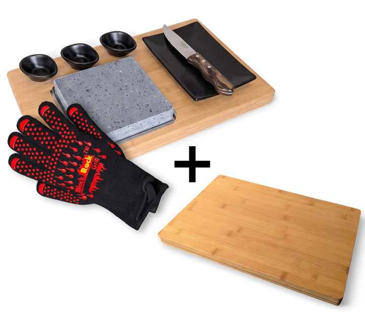Black rock grill steak on the stone set including lava cooking stone black ceramic dipping pots, side plate, gloves and a knife on a bamboo serving platter. with a plus symbol indicating a set with a bamboo cutting board shown on a white background.