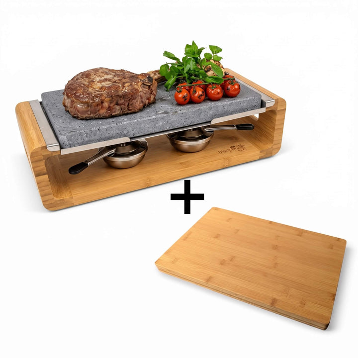 The Black Rock Grill Steak Stone Sharing Platter &amp; Grill Set by Black Rock Grill features a tabletop lava rock grill displaying steak, tomatoes, and herbs, accompanied by two small bowls below and a separate complimentary bamboo cutting board (worth £19.99), all set against a white background.