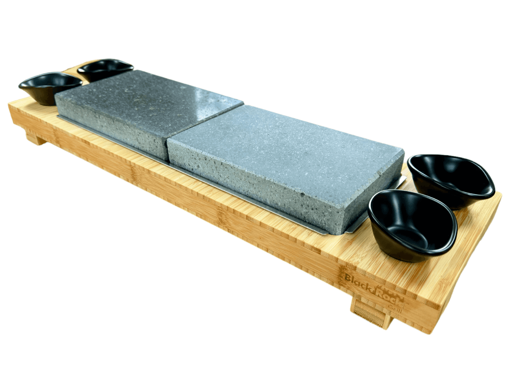 The Black Rock Grill Signature Steak Sharing Stone Set features a FREE rectangular bamboo board (worth £19.99), two large gray stone slabs positioned at the center, and four small black sauce bowls in each corner, delivering a restaurant-quality steak stone presentation perfect for an unforgettable dining experience.