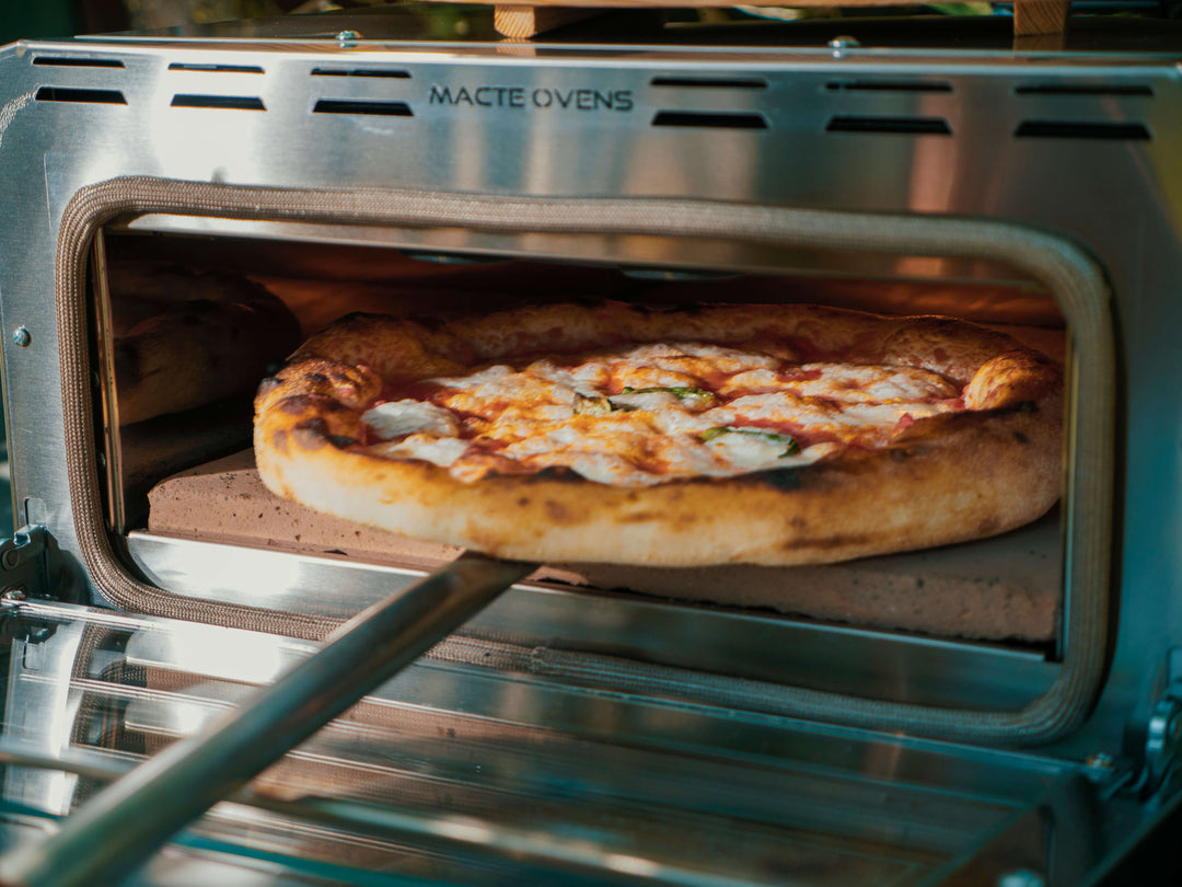 A freshly baked pizza being removed from the open Macte Voyager Twin Advanced pizza oven.